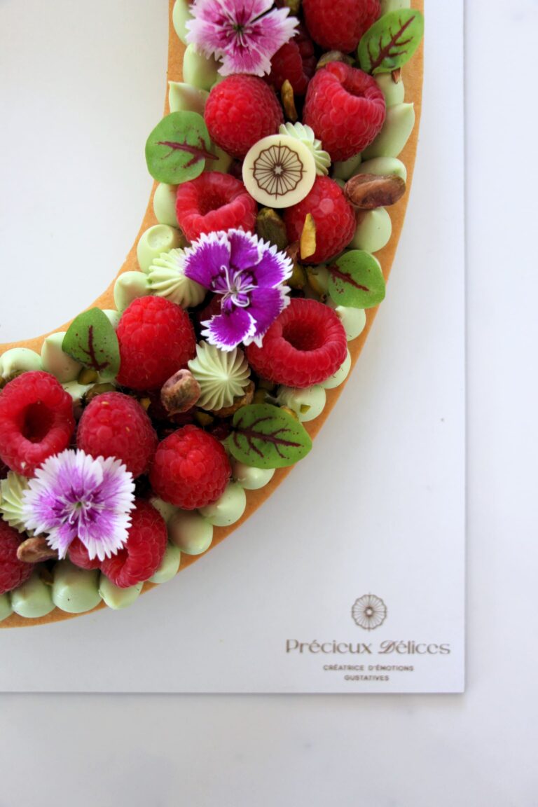 Gros plan sur un Number Cake pistache framboise garni de framboises fraîches, crème pistache, éclats de pistaches et fleurs comestibles, réalisé par Précieux Délices à Orléans.