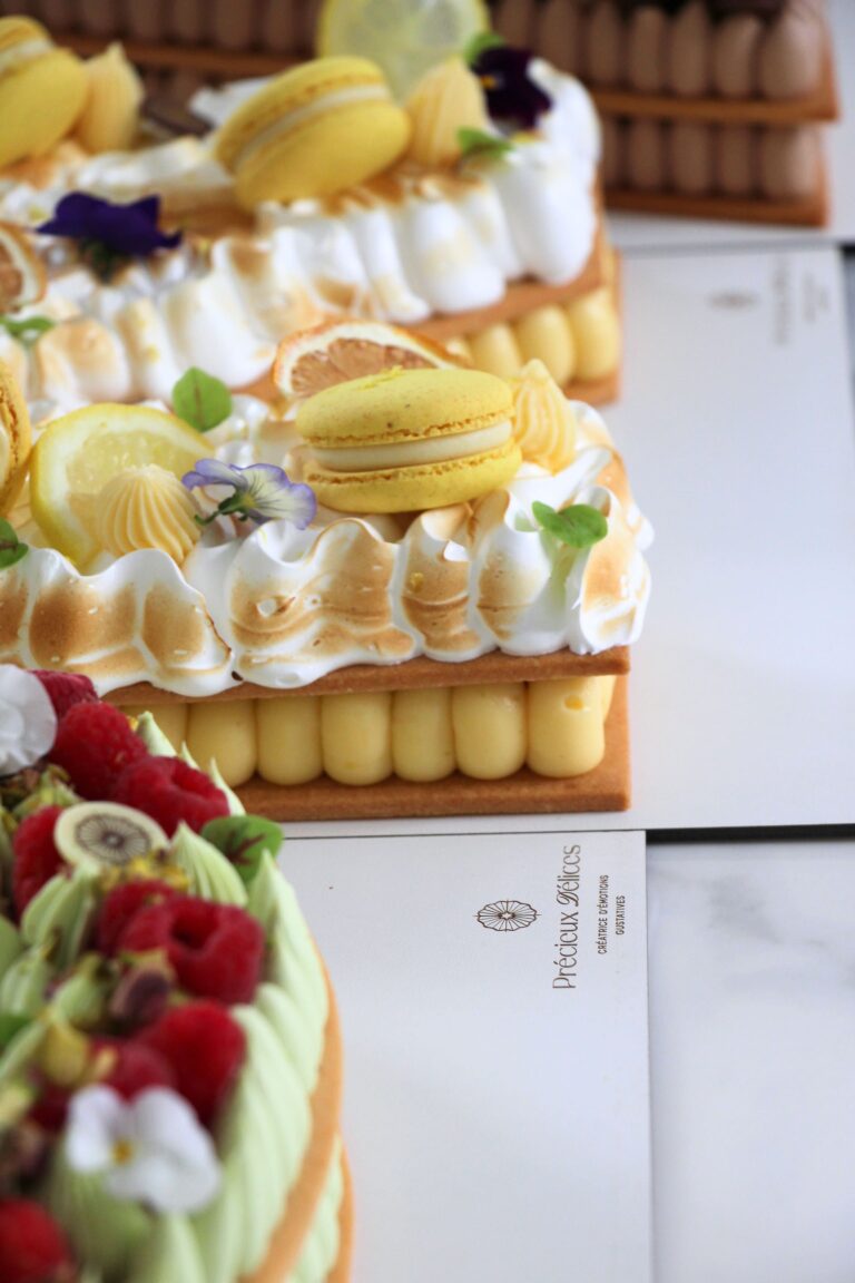 Gros plan sur un Number Cake citron meringué décoré de meringue italienne dorée, macarons au citron, rondelles de citron et fleurs comestibles.